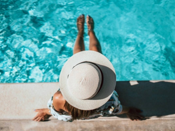 Vue en plongée d'une femme portant un chapeau de paille, relaxant au bord d'une piscine chauffée turquoise dans un camping à vendre en Montérégie, près de Montréal.