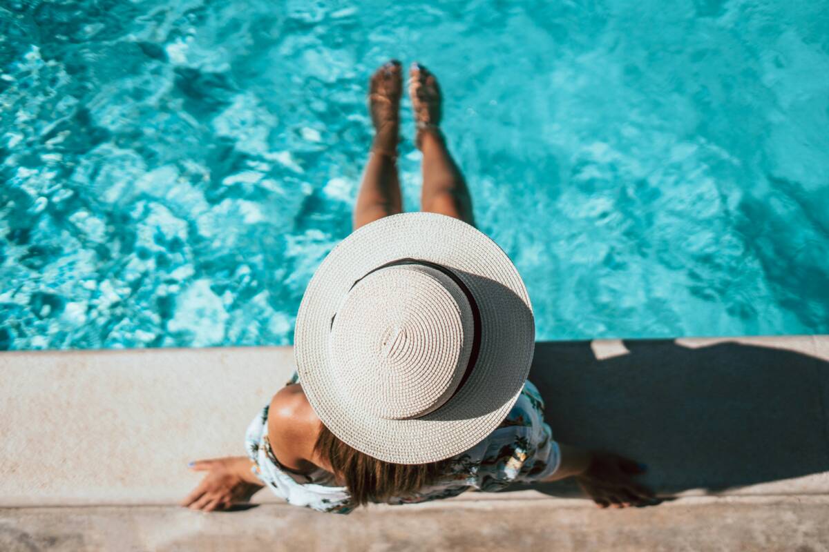 Vue en plongée d'une femme portant un chapeau de paille, relaxant au bord d'une piscine chauffée turquoise dans un camping à vendre en Montérégie, près de Montréal.