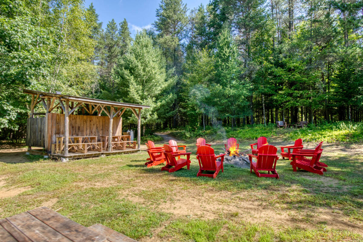 Espace commun de feu de camp avec chaises et abri. Un site de camping à vendre dans les Laurentides, près de Mont-Tremblant