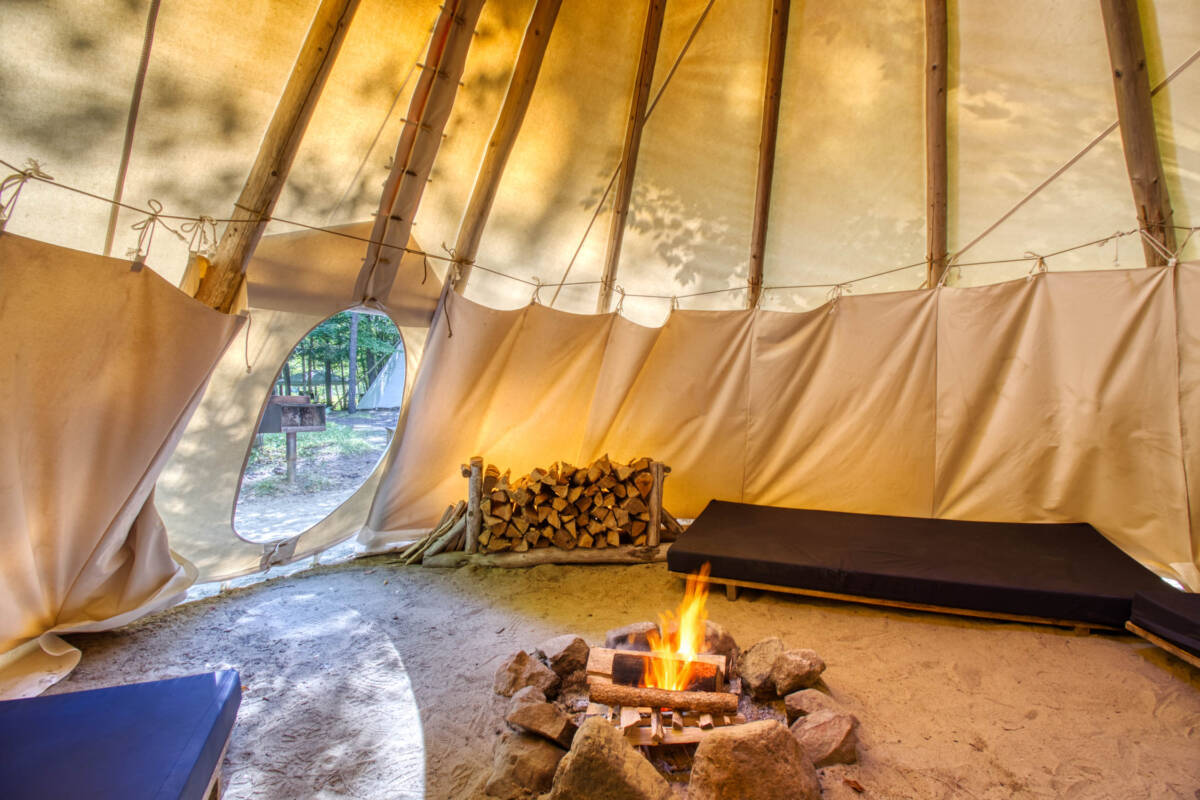 Intérieur d'un tipi avec un foyer au sol. Un site de camping-glamping à vendre dans les Laurentides, près de Mont-Tremblant, qui offre une expérience unique