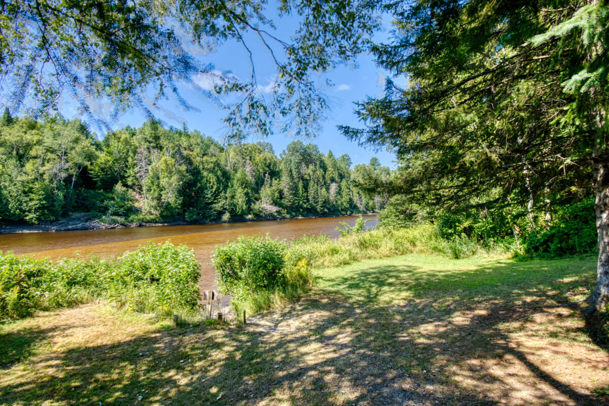 Accès à la Rivière Rouge de ce camping à vendre dans les Laurentides, près de Mont-Tremblant. Terrain gazonné et arbres matures