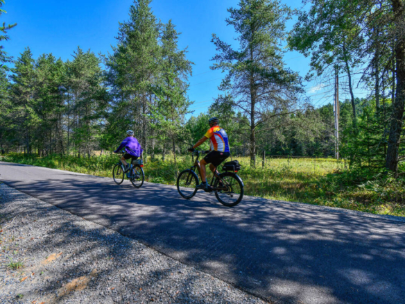 Cyclistes sur la piste asphaltée du Petit Train du Nord, un sentier qui longe un camping à vendre dans les Laurentides, près de Mont-Tremblant