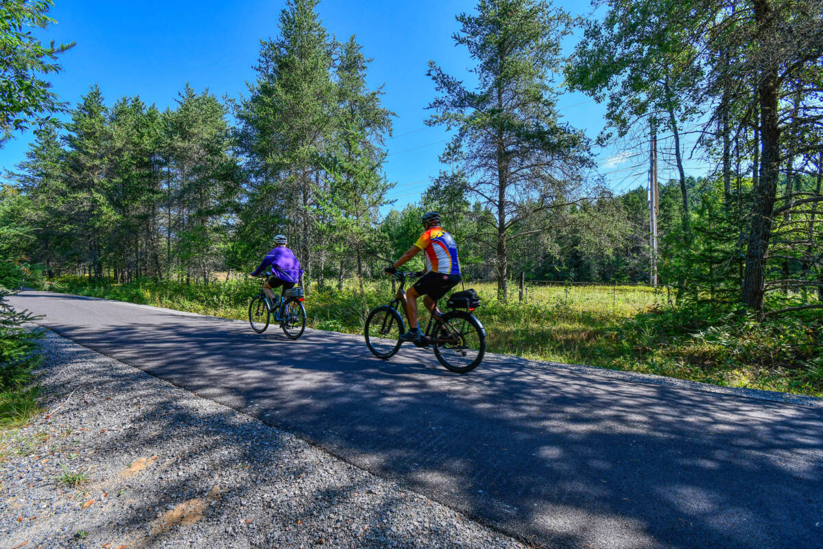 Cyclistes sur la piste asphaltée du Petit Train du Nord, un sentier qui longe un camping à vendre dans les Laurentides, près de Mont-Tremblant