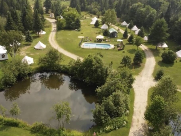 Texte alternatif : Vue aérienne d'un domaine de glamping à vendre avec piscine, étang et tentes aménagées près de Mont-Tremblant.