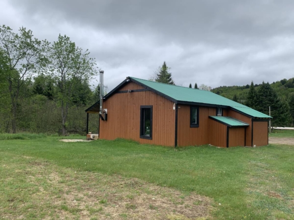 Extérieur du chalet en bois avec toit vert sur le domaine de glamping à vendre à Mont-Tremblant.