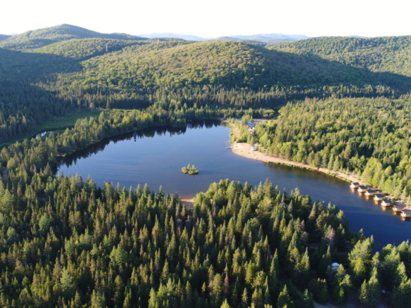 Vue aérienne panoramique du Domaine Lausanne montrant le lac privé en forme de cœur entouré d'une forêt boréale dense avec une rangée de cabines flottantes sur la rive.