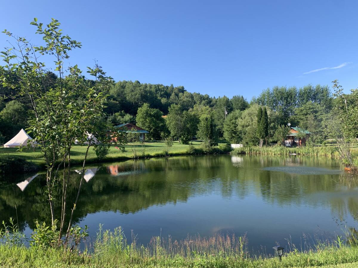 Étang Privé du Domaine de Glamping à Vendre Étang naturel reflétant les arbres, les tentes de glamping et les bâtiments du domaine à vendre près de Mont-Tremblant.