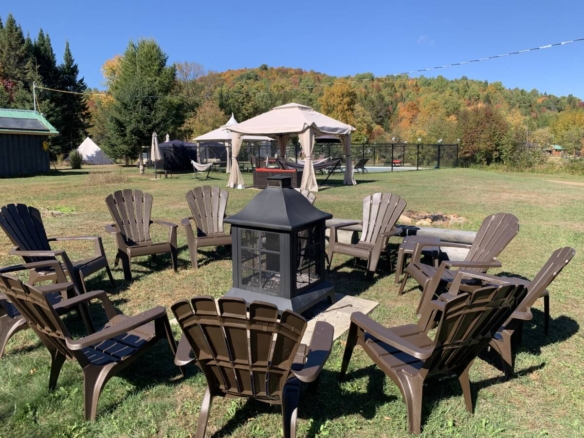 Foyer extérieur noir entouré de chaises Adirondack brunes sur un domaine de glamping à vendre près de Mont-Tremblant.