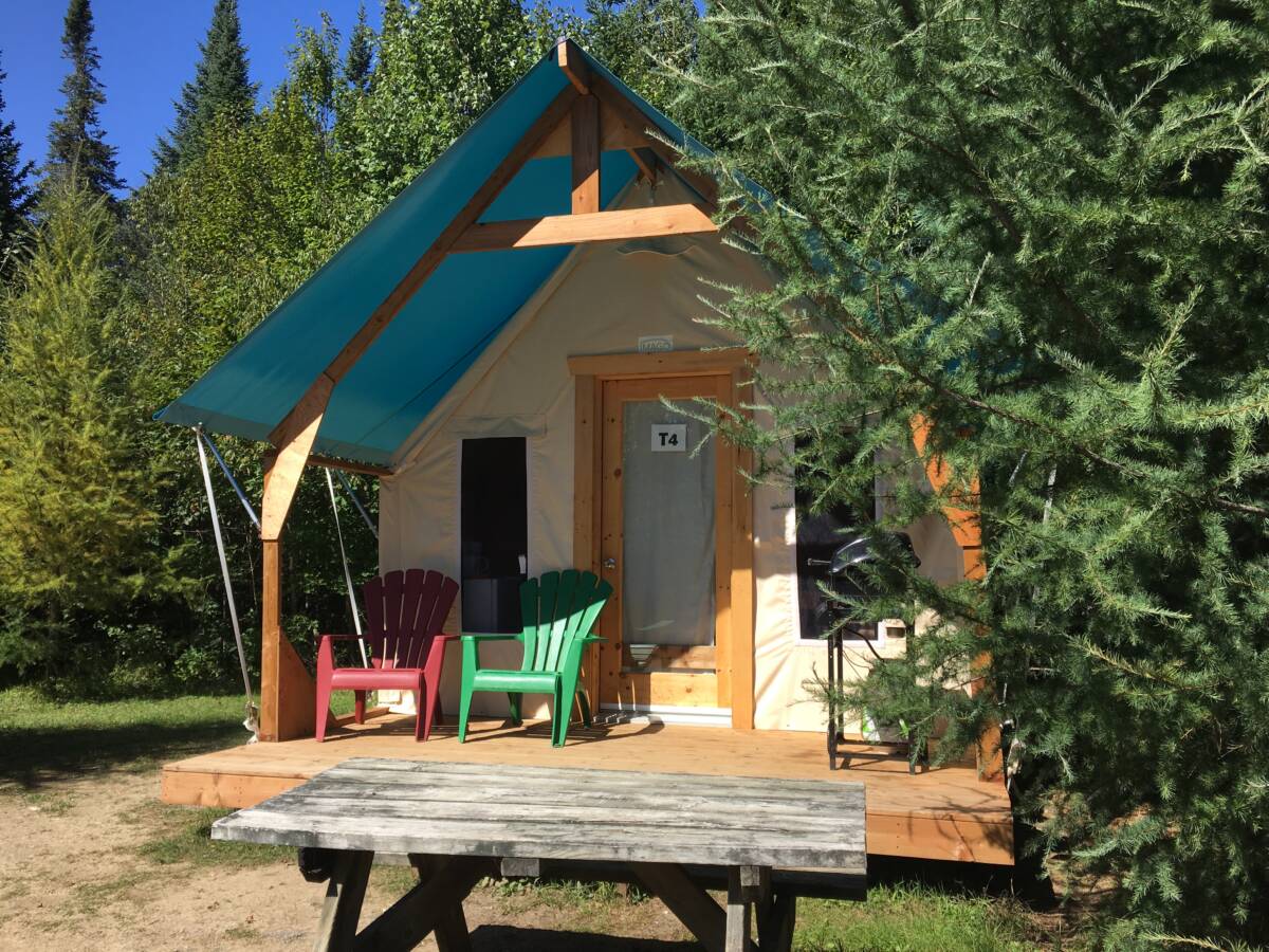 Une tente de prêt-à-camper de style prospecteur avec un toit turquoise et une terrasse en bois équipée de deux chaises Adirondack (une rouge et une verte) au Domaine Lausanne.