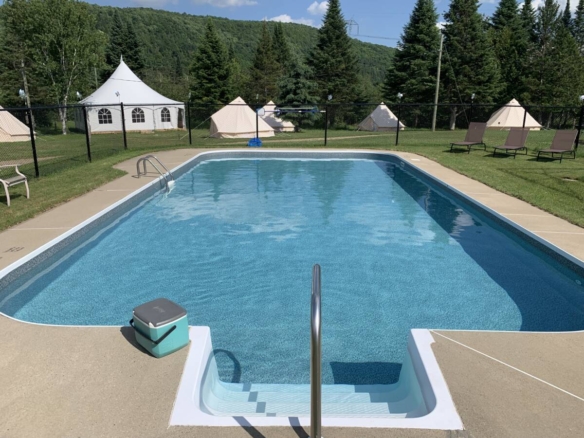 Piscine creusée chauffée et clôturée avec chaises longues et tentes de glamping en arrière-plan à vendre près de Mont-Tremblant.