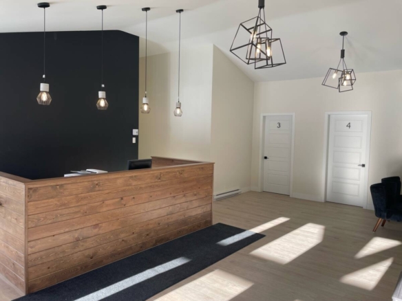 L'intérieur moderne du pavillon de réception avec un comptoir en bois, un mur d'accent noir mat et des luminaires suspendus géométriques dans un domaine privé.