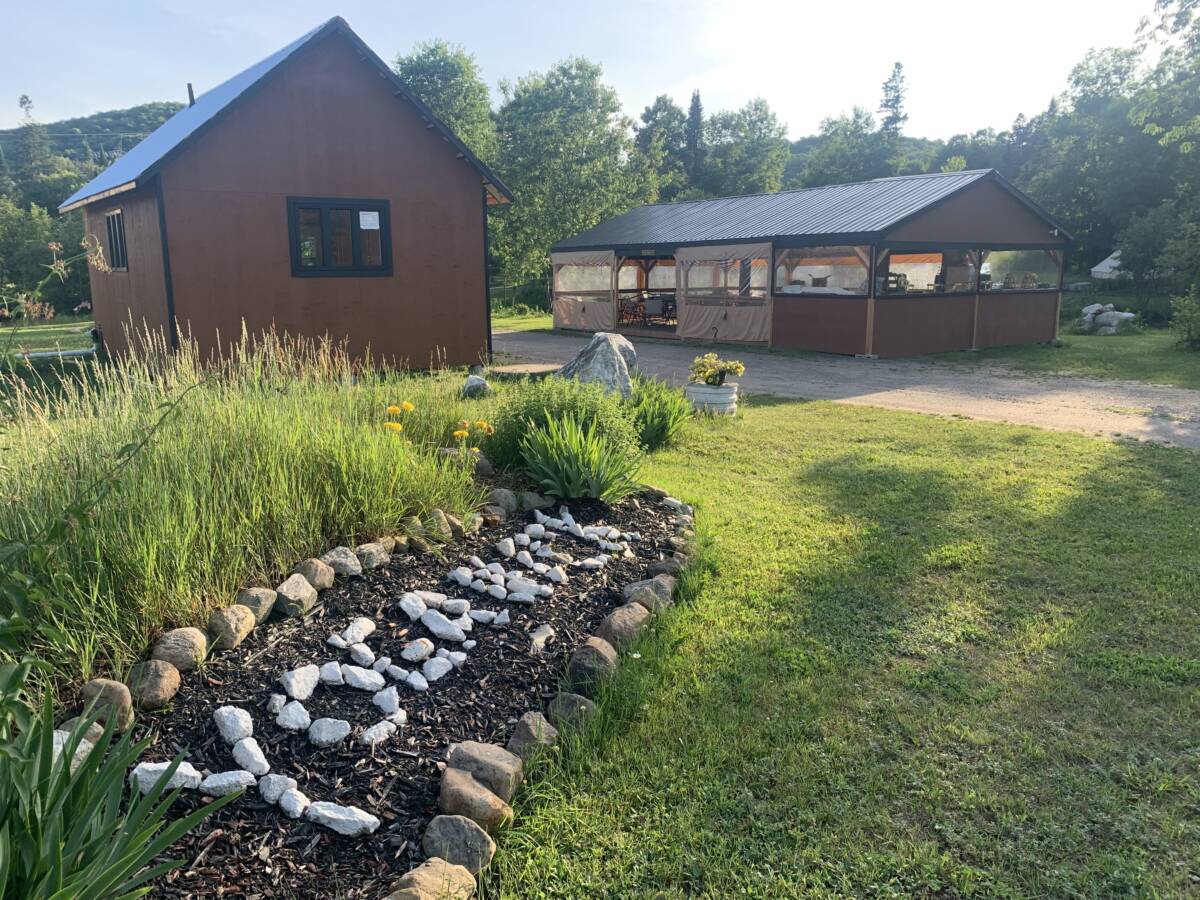 Accueil et pavillon communautaire du domaine de glamping à vendre Bâtiments en bois brun et aménagement paysager avec le mot « PAIX » écrit en pierres blanches sur un domaine de glamping à vendre.