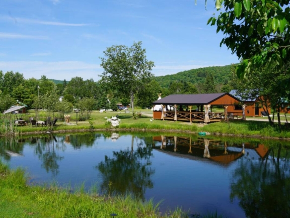 Vue paisible de l'étang reflétant le pavillon en bois et la forêt sur un domaine de glamping à vendre près de Mont-Tremblant.