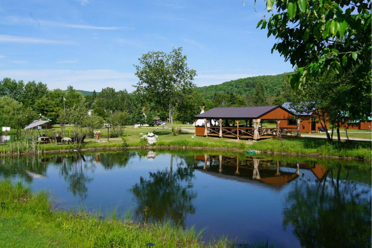 Paysage avec étang et pavillon – Domaine touristique à vendre Vue paisible de l'étang reflétant le pavillon en bois et la forêt sur un domaine de glamping à vendre près de Mont-Tremblant.