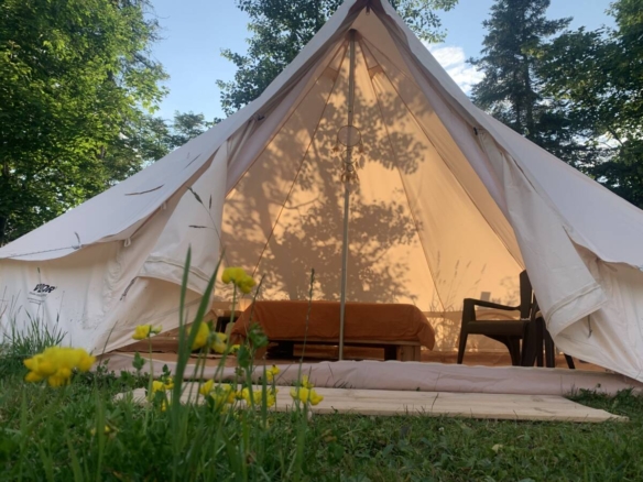 Intérieur d'une tente de glamping lumineuse avec lit double et fauteuil dans un domaine à vendre près de Mont-Tremblant