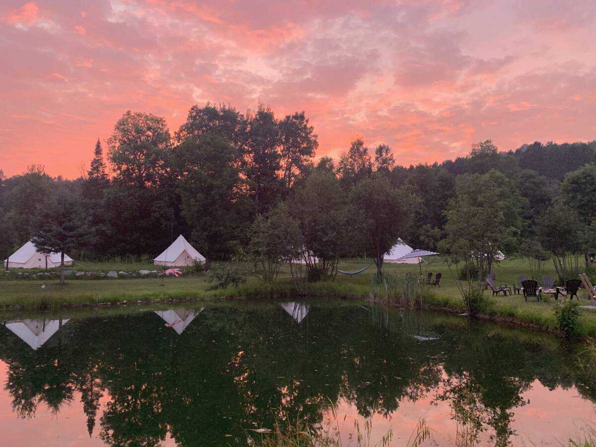 Coucher de soleil sur l’étang du centre de ressourcement – Mont-Tremblant Coucher de soleil flamboyant aux teintes roses et orangées se reflétant dans l'étang d'un domaine de glamping à vendre près de Mont-Tremblant.